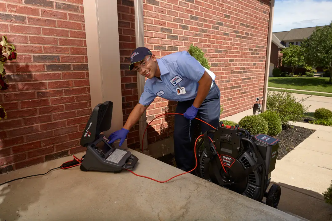 Plumber smiling and pointing to HDTV monitor while conducting video camera sewer line inspection